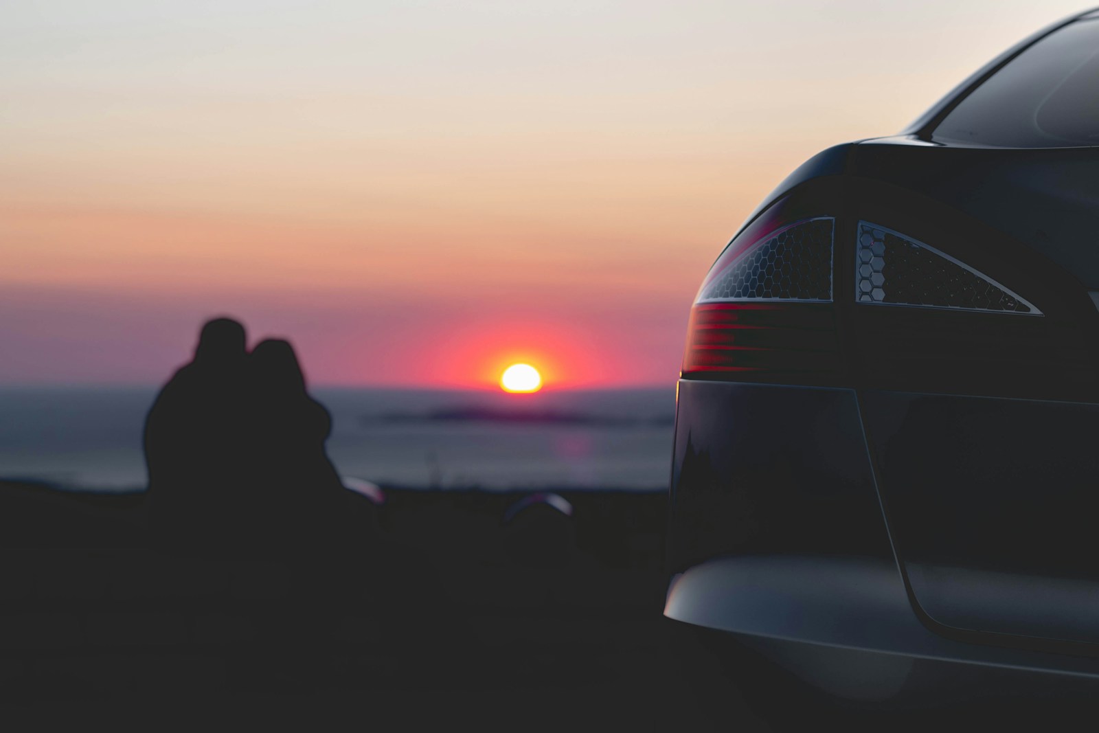 couple sitting near body of water watching sunset with auto